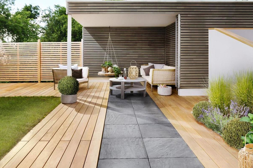 Großzügige Holzterrasse mit Sichtschutzwand und Lounge-Ecke, kombiniert mit Gehweg aus Steinplatten.
