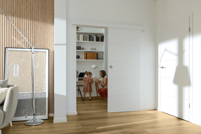 Weiße Schiebetür mit Griffmuschel vor kleinem Arbeitszimmer.