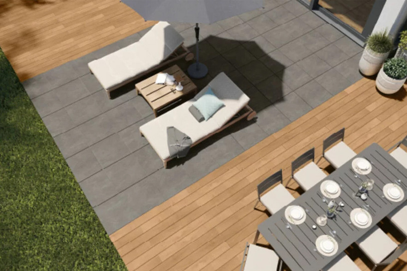Moderne Terrasse mit großformatigen Fliesen, Holzbelag, Sonnenliegen und Esstisch unter einem Sonnenschirm.