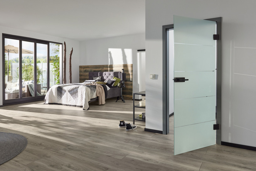 Matte Ganzglastür mit schwarzen Beschlägen im modernen Schlafzimmer.