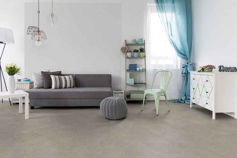 Minimalistisch eingerichtetes Wohnzimmer mit grauem Sofa, hellgrauem Korkboden in Steinoptik und Akzenten in Pastellfarben.